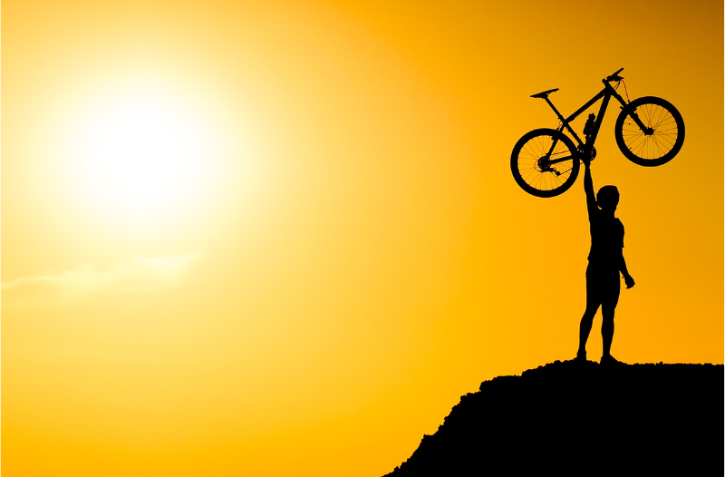 Homem equilibra bicicleta com um braço, ao fundo imagem do sol.